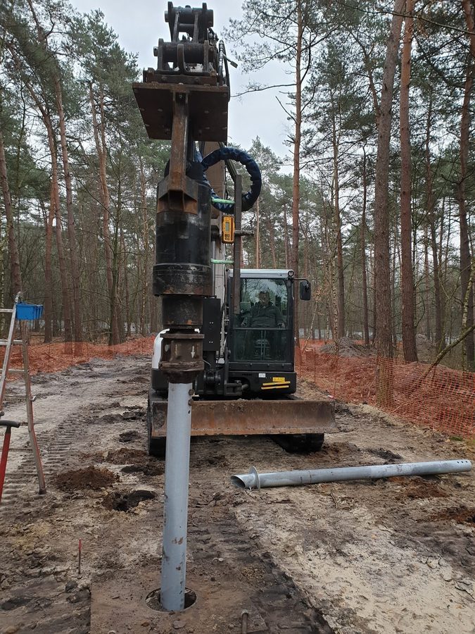 Excavadora instalando un pilote helicoidal galvanizado entre los pinos del bosque de Bosland, Bélgica