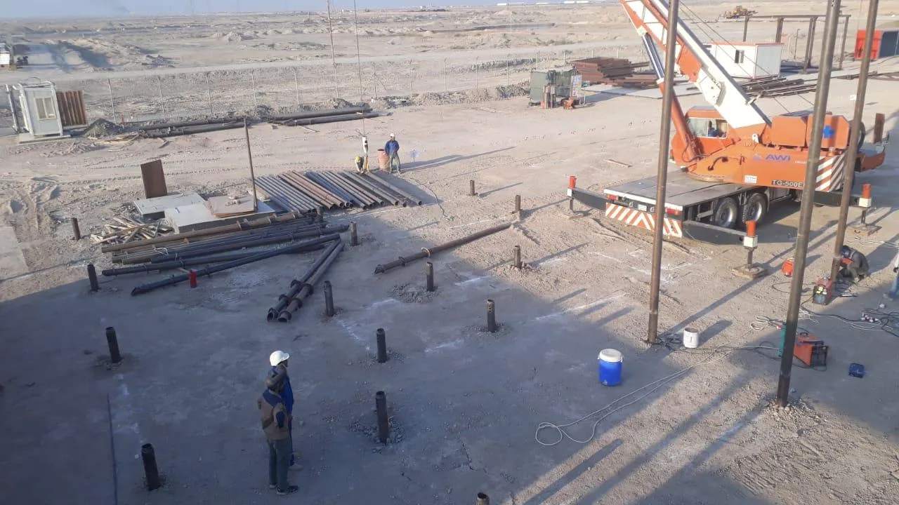 Instalación de pilotes helicoidales con grúa en el yacimiento petrolífero de Basora, operarios posicionando pilotes helicoidales en condiciones de desierto